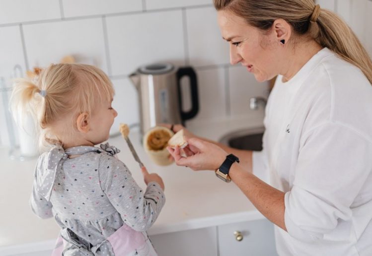A mother and her young daughter interact while preparing food in a modern kitchen.