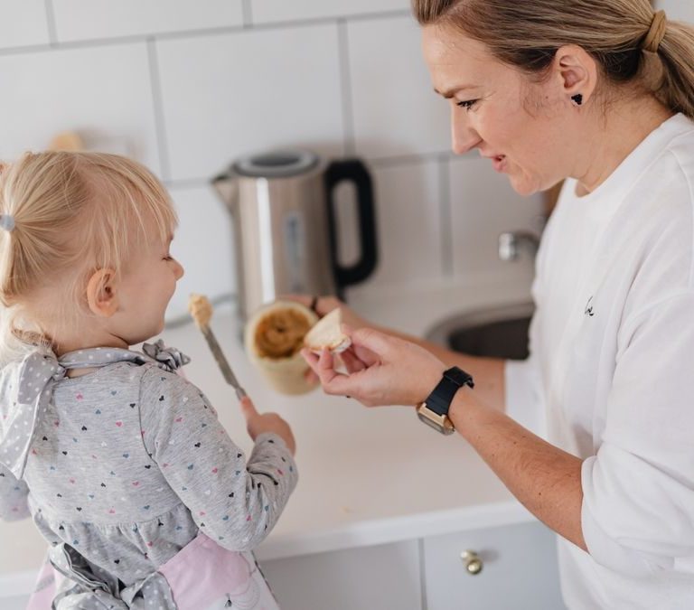 A mother and her young daughter interact while preparing food in a modern kitchen.