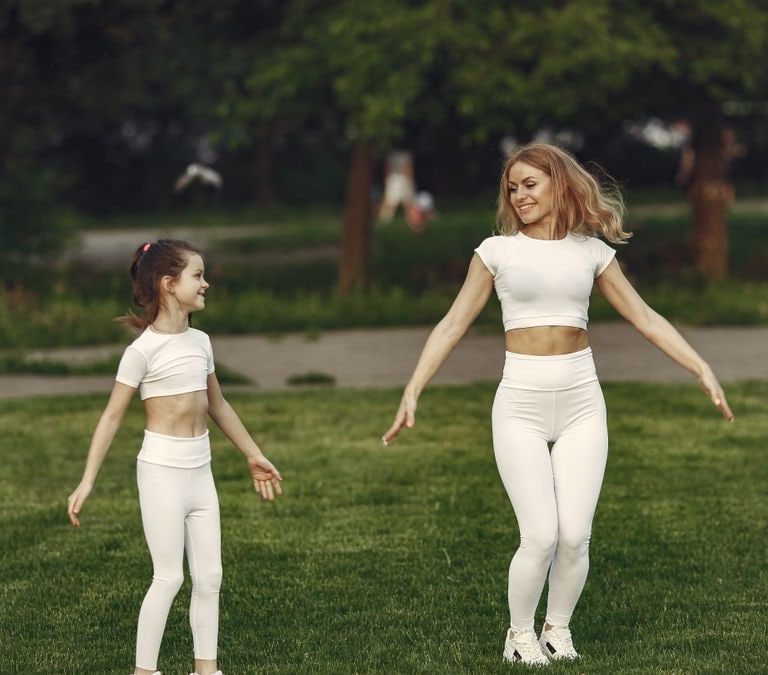 Mother and daughter bonding through outdoor exercise in activewear, featuring a joyful moment in a green park.